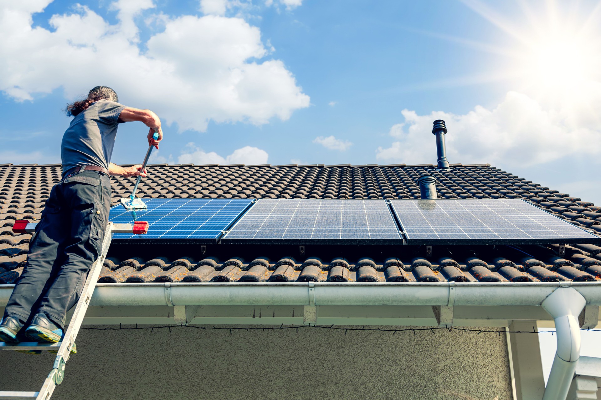Balkonkraftwerk 600w in Germany. man holding mop cleaning solar panels. cleaning of solar modules with water. close-up of solar panels on the roof on sunny sky. Mop cleaning. Washing Solar modules in summer season on sunny day.